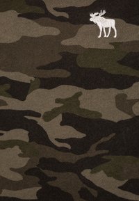 Tela con patrón de camuflaje en tonos de verde y marrón, con un silueta de alce blanca bordada. Acabado texturizado y suave.