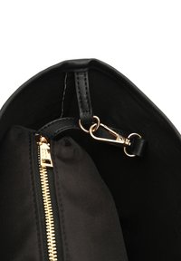 Czarna torebka wewnątrz z złotym zamkiem, czarną podszewką i metalowym klipsem do mocowania przedmiotów. Gładka faktura i prosty design.