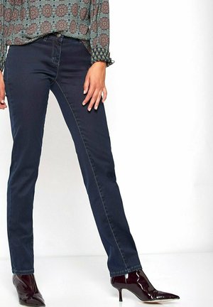 Dunkelblaue Jeans mit schlankem Schnitt, ausgestattet mit dezenten Stichdetails. Kombiniert mit glänzenden, spitzen Absätzen für einen Kontrast.