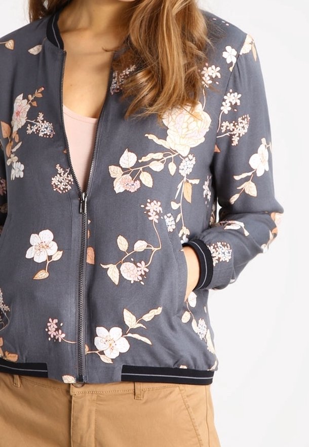 Giubbotto bomber floreale grigio con fiori bianchi e pesco, polsini a coste, chiusura con zip e una texture in tessuto morbido.
