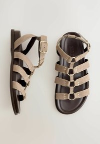 Beige Wildleder-Gladiator-Sandalen mit mehreren Riemen, Schnalle in Goldoptik und dunkelbrauner Sohle, von oben auf hellem Hintergrund dargestellt.