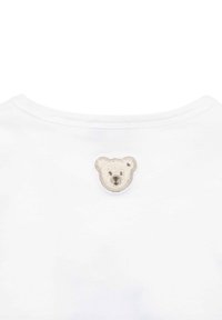 T-shirt bianco in cotone con un volto di orso ricamato beige e marrone sul collo posteriore. Texture morbida e design con colletto rotondo.