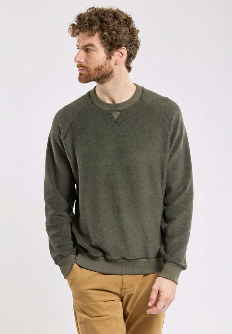 Sweatshirt vert olive, tissu texturé, encolure ronde, poignets et ourlet côtelés, manches raglan, porté avec un pantalon beige.