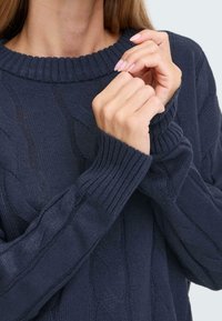 Maglione blu navy a trecce con scollo rotondo a costine e polsini. La texture presenta motivi a spirale in rilievo lungo le maniche e il corpo.