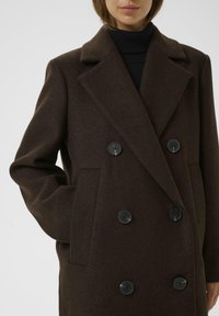 Manteau en laine mélangée marron avec un design croisé, de grands boutons noirs et des revers à cran ; possède des poches latérales et une coupe structurée.