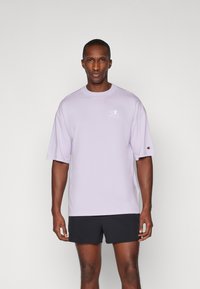 Lilla kortærmet t-shirt lavet af bomuld, med rund halsudskæring og et lille logo på brystet. Sæt sammen med sorte shorts.