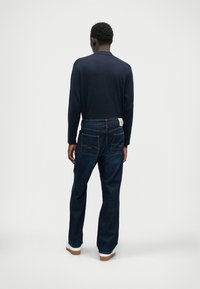 Ναυτικό μπλουζάκι με μακριά μανίκια, σκούρες μπλε τζιν με πίσω τσέπες, διακριτές ραφές και λευκά αθλητικά παπούτσια. Απλός, άνετος σχεδιασμός.