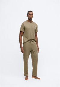 Olívazöld kényelmi ruházat, rövid ujjú, kerek nyakú pólóval és rugalmas derékpántos, húzózsinóros nadrággal.