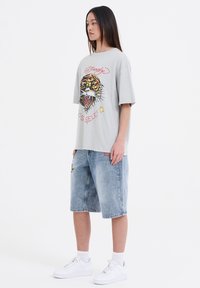 Lys grå oversized t-shirt med tiger grafisk tryk; parret med knælange, slidte blå denimshorts og hvide sneakers.