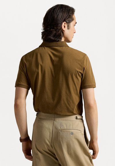 Brown polo shirt with a collar and short sleeves, textured cotton fabric, paired with beige trousers, featuring a back pocket and button detail.