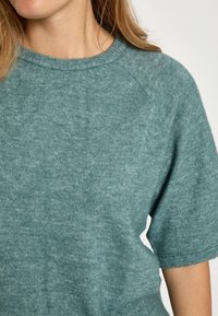 Svetlomodrý krátky rukáv sveter vyrobený z mäkkého materiálu. Má okrúhly výstrih a mierne štruktúrovaný povrch.