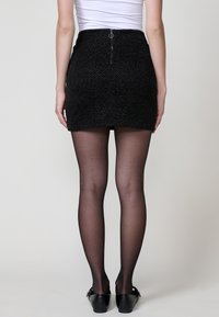 Zwarte minirok van textuurstof, met een hoge taille, ritssluiting aan de achterkant en een strakke pasvorm, gecombineerd met doorzichtige zwarte panty en flats.