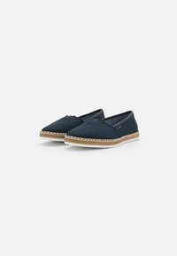 Navy canvas slip-on shoes with a flat, round toe, contrasting tan woven midsoles, and white stitching along the edge.