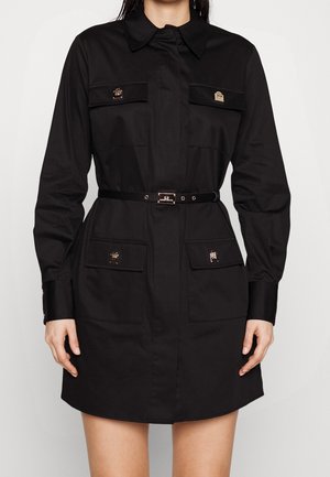 Sort langærmet skjortekjole med krave, fire forlommer med klapper og metalspænder, samt et tyndt sort bælte i taljen.