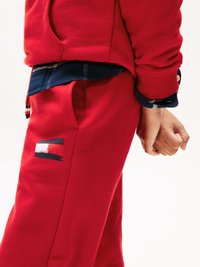 Rode katoenen sweatshirt met ribbelmanchetten, gedragen over een marineblauw geruit shirt. Opvallend logodetail met rode, witte en blauwe penseelstreken op de broek.