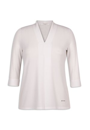 Blouse blanche à manches longues avec un col en V, dotée d'une coupe droite et d'un léger pli sur le devant. Les poignets sont retroussés, avec un petit accent en logo argenté.