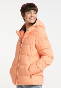 Giacca a vento arancione con cappuccio, caratterizzata da sezioni trapuntate e un logo a forma di cuore sul petto. Tasche con zip e tirazip a forma di cuore.