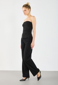 Top nero senza spalline con texture arricciata, abbinato a pantaloni wide-leg neri. Completato da décolleté nere a punta con pois bianchi.