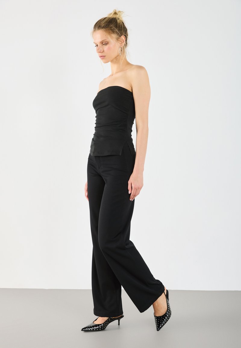 Top noir sans bretelles avec texture froncée, associé à un pantalon large noir. Complété par des talons aiguille noirs avec des pois blancs.