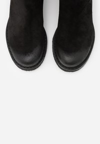 Bottines noires avec une finition en daim mat, bout rond et semelle en caoutchouc robuste. Lignes épurées et détails de couture minimalistes.