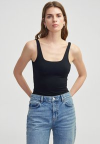 Černý bezrukávový bodysuit se čtvercov�ým výstřihem, spárovaný s vysokými světle modrými džíny, které mají hladkou texturu a minimální detaily.