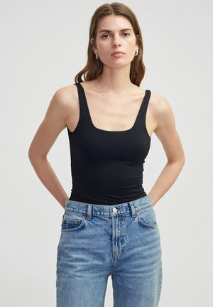Zwarte mouwloze bodysuit met een vierkante halslijn, gecombineerd met lichtblauwe highwaisted denim jeans, die een gladde textuur en minimale details accentueren.