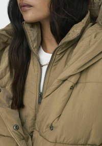 Olivově zelená péřová bunda s jemným leskem a texturou, s vysokým límcem, zapínáním na zip a velkými kapsami na knoflík.