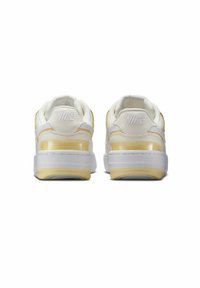 Zapatillas Nike blancas y doradas que presentan un exterior de cuero suave, un cuello acolchado y una suela de goma blanca con un acento amarillo translúcido.