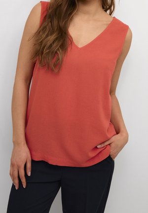 Coral sleeveless top with a V-neck design, made of soft fabric. Features a relaxed fit and a straight hemline, paired with black pants.