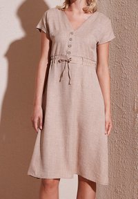 Robe en lin marron clair avec un décolleté en V, des manches courtes, un devant à boutons et une ceinture ajustable à la taille. Présente une coupe évasée fluide et une texture lisse.