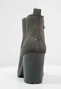 Stivale alla caviglia in suede grigio con un pannello in tessuto testurizzato, tacco alto nero, chiusura con zip e piccolo logo laterale.