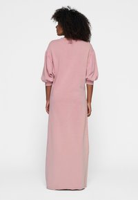 Lange, roze jurk van een zachte stof met pofmouwen en een ronde hals. Heeft een losse pasvorm en zijsplitten voor bewegingsgemak.