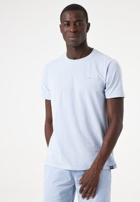 Camiseta de algodón azul claro con cuello redondo y mangas cortas. Presenta un pequeño logo en el pecho y un corte relajado.