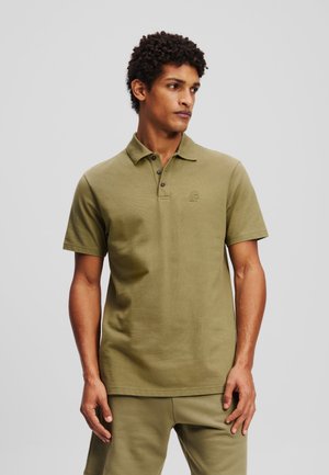 Olivgrünes Poloshirt aus strukturiertem Baumwollstoff mit einer Knopfleiste mit drei Knöpfen und einem gestickten Logo auf der Brust. Kurze Ärmel und eine lockere Passform.