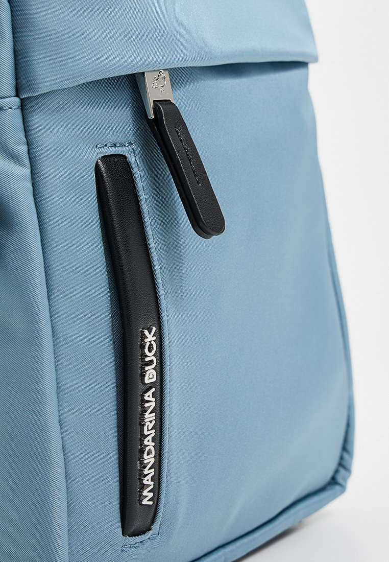 Hellblauer Rucksack mit schwarzen Akzenten, ausgestattet mit einem oberen Reißverschluss und einer Seitentasche. Das Material hat eine glatte Textur, das Logo ist sichtbar.