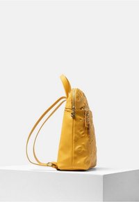 Yellow leather backpack with embossed logo, designed with a side zip, adjustable straps, and layered decorative charms.