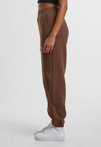 Bruine katoenen sweatpants met een elastische tailleband, zijzakken en taps toelopende manchetten, gecombineerd met witte sneakers.