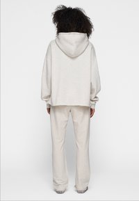 Sudadera de gran tamaño en gris claro con capucha y hombros caídos, combinada con pantalones de corte relajado a juego, ambos fabricados en un tejido suave y texturizado.