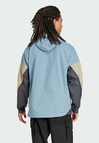 Chaqueta con capucha de cuadros en azul claro, con mangas en beige y azul oscuro en contraste. Presenta puños elásticos y un corte holgado.