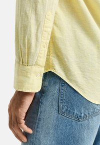 Geel linnen overhemd met een knoopmanchet en een zachte textuur, gecombineerd met blauwe denim jeans met een achterzak en een taps toelopende vorm.