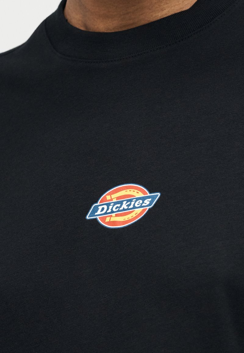 Primo piano di una maglietta nera con scollo rotondo e un piccolo logo colorato "Dickies" sul petto.