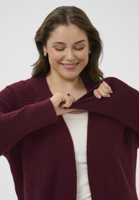 Cardigan borgogna a coste con maniche lunghe e un ampio davanti aperto, caratterizzato da una texture morbida e una vestibilità casual.