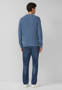 Blauer Strickpullover mit strukturierter Oberfläche, Rundhalsausschnitt und langen Ärmeln, kombiniert mit dunklen Denim-Jeans und weißen Turnschuhen.