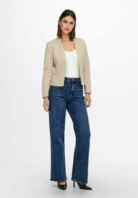 Beige bleiseri med strukturell design, kombinert med høyt liv blå denimjeans med lommer. Sorte spisse hæler fullfører stilen.