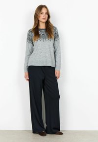 Pulover gri tricotat cu modele geometrice negre în partea superioară, asortat cu pantaloni negri cu croială largă și pantofi slip-on maro.