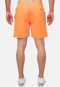 Costumi da bagno arancioni con fascia elastica in vita, due tasche laterali e una tasca posteriore. Materiale testurizzato e lunghezza sopra il ginocchio.