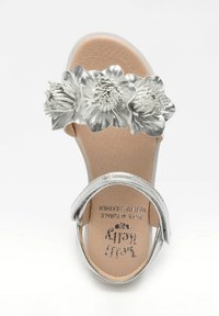 Sandalo in pelle argento con decorazioni floreali sulla fascia, soletta imbottita e una larga cinghia alla caviglia. Suola piatta per il massimo comfort.