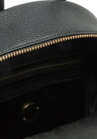 Interno di una borsa a tracolla in pelle nera con zip dorata, rivestimento morbido nero e una piccola tasca con zip. Presenta un dettaglio del logo circolare.