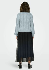 Pull en maille torsadée bleu clair à manches longues, associé à une jupe maxi plissée noire et des chaussures à talons noires avec des accents en ruban.
