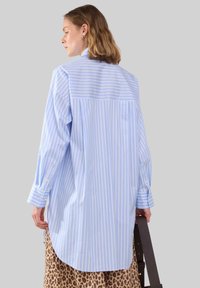 Lys blå og hvid stribet oversized skjorte med lange ærmer og rundet kant, parret med en leopardprintet nederdel.